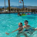 Happy children play in a swimming pool under a sunny sky.