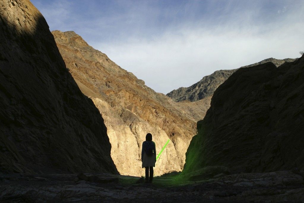A silhouette of a person standing in Death Valley, holding a green light saber.