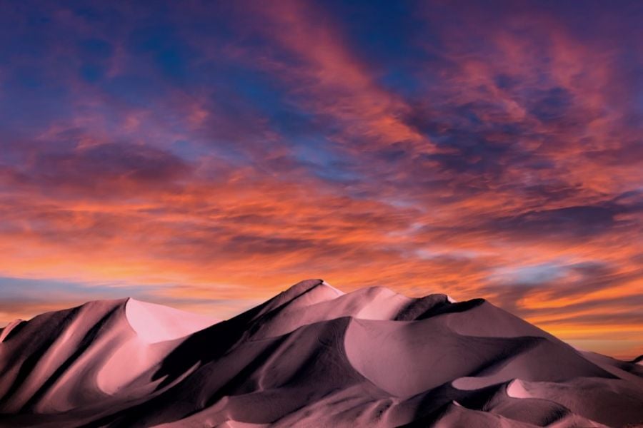 An orange and pink sunset over windswept sand dunes.