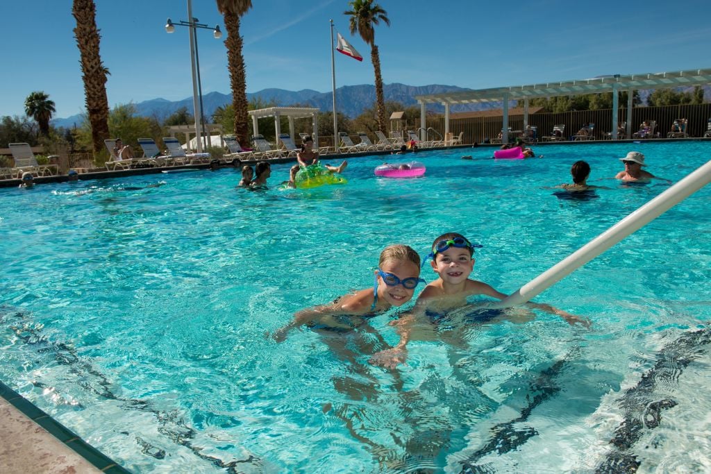 Happy children play in a swimming pool under a sunny sky.