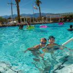 Happy children play in a swimming pool under a sunny sky.