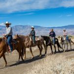 A group of five men traverse the desert on horseback.